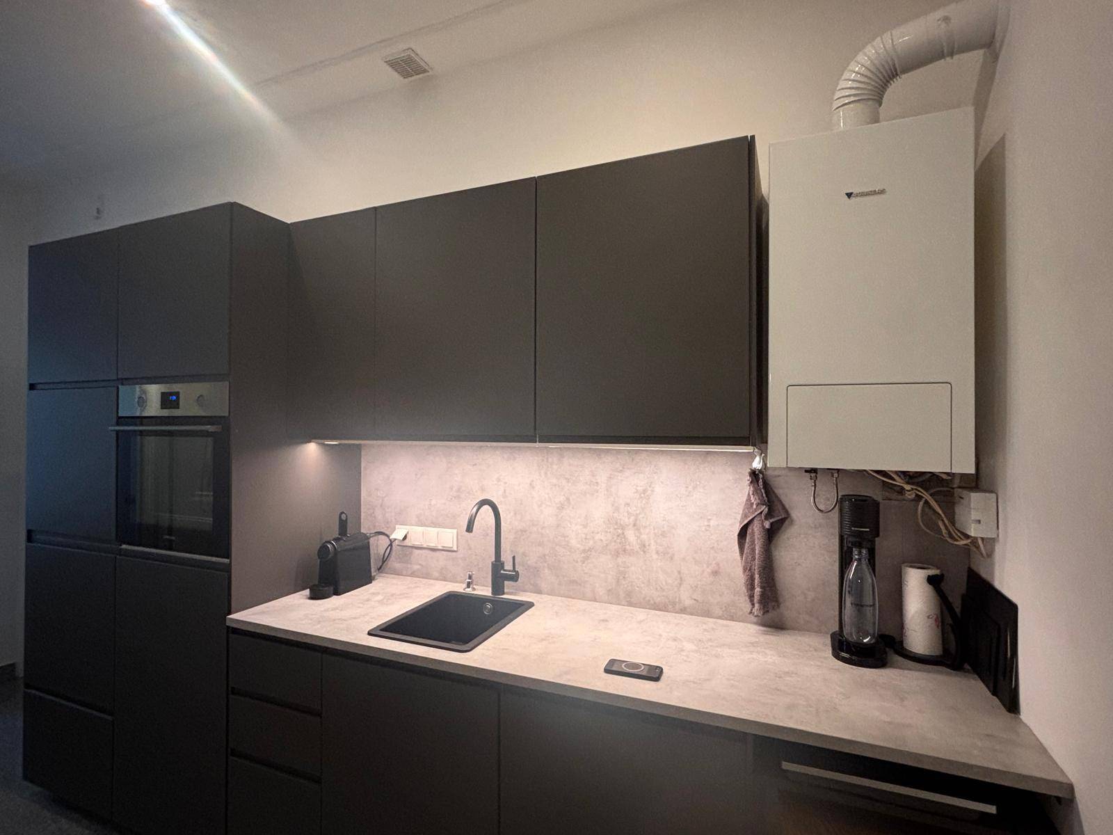 Moderne Küche mit dunklen Schränken, integriertem Backofen und einer Arbeitsplatte in Betonoptik.