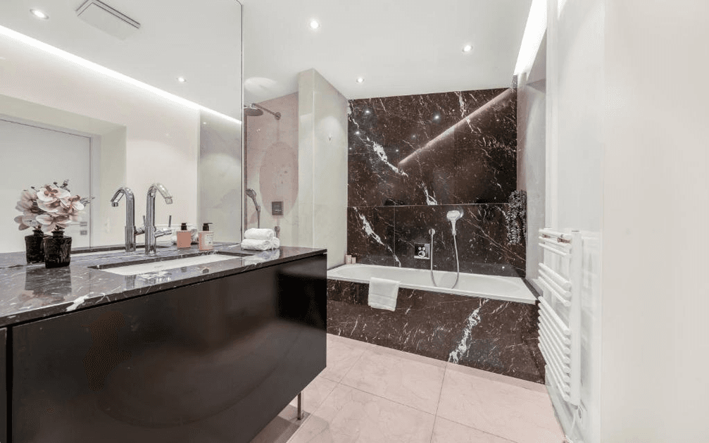 Luxuriöses Badezimmer mit dunklen Marmoroberflächen, Badewanne, Dusche und beheiztem Handtuchhalter.