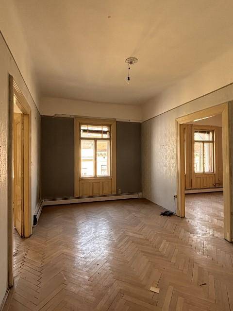 Helles Zimmer mit Fischgrätparkett und hohen Fenstern, das auf eine Renovierung wartet.