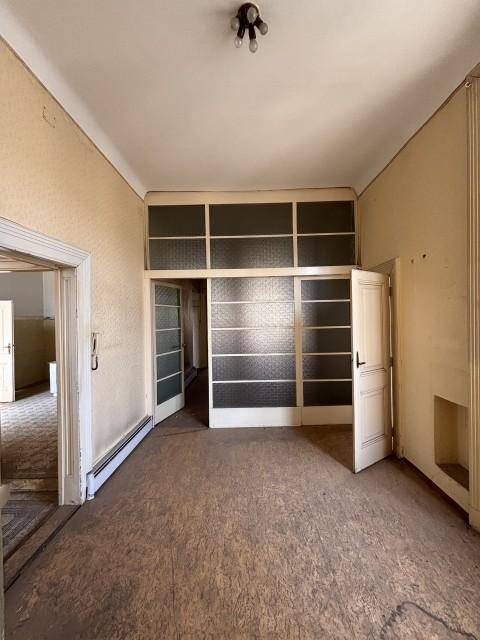 Geräumiges Zimmer mit alten Holzböden und einer Trennwand mit Glasfenstern, die auf einen Flur führt.