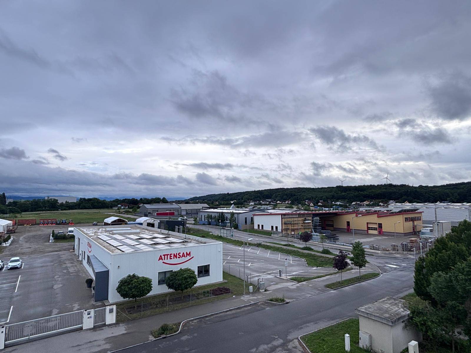 Weitläufiger Blick über ein Gewerbegebiet und die umliegende Landschaft unter bewölktem Himmel.