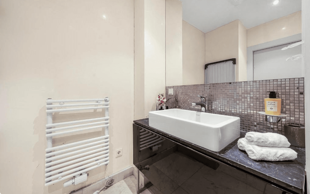 Modernes Badezimmer mit Einzelwaschbecken, beheiztem Handtuchhalter und Spiegelschrank.