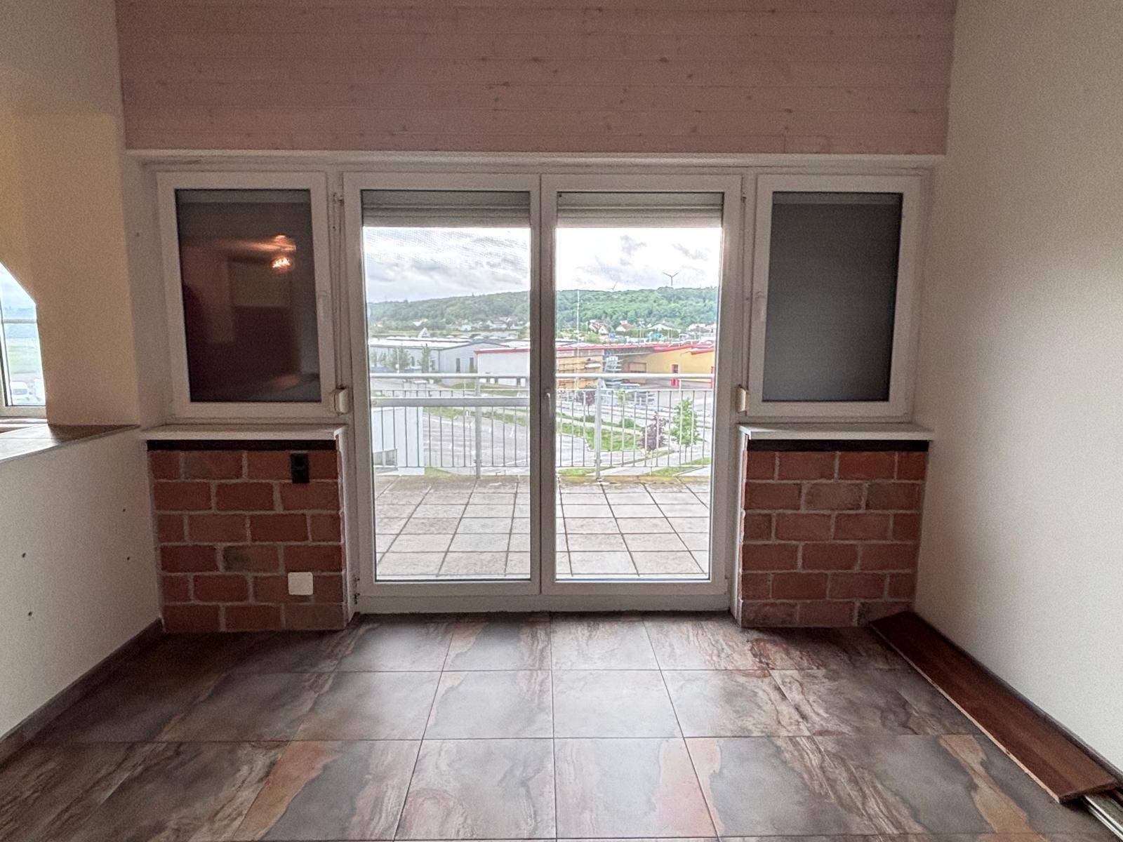 Raum mit Fliesenboden und großen Schiebetüren, die zu einem Balkon mit weitem Blick führen.
