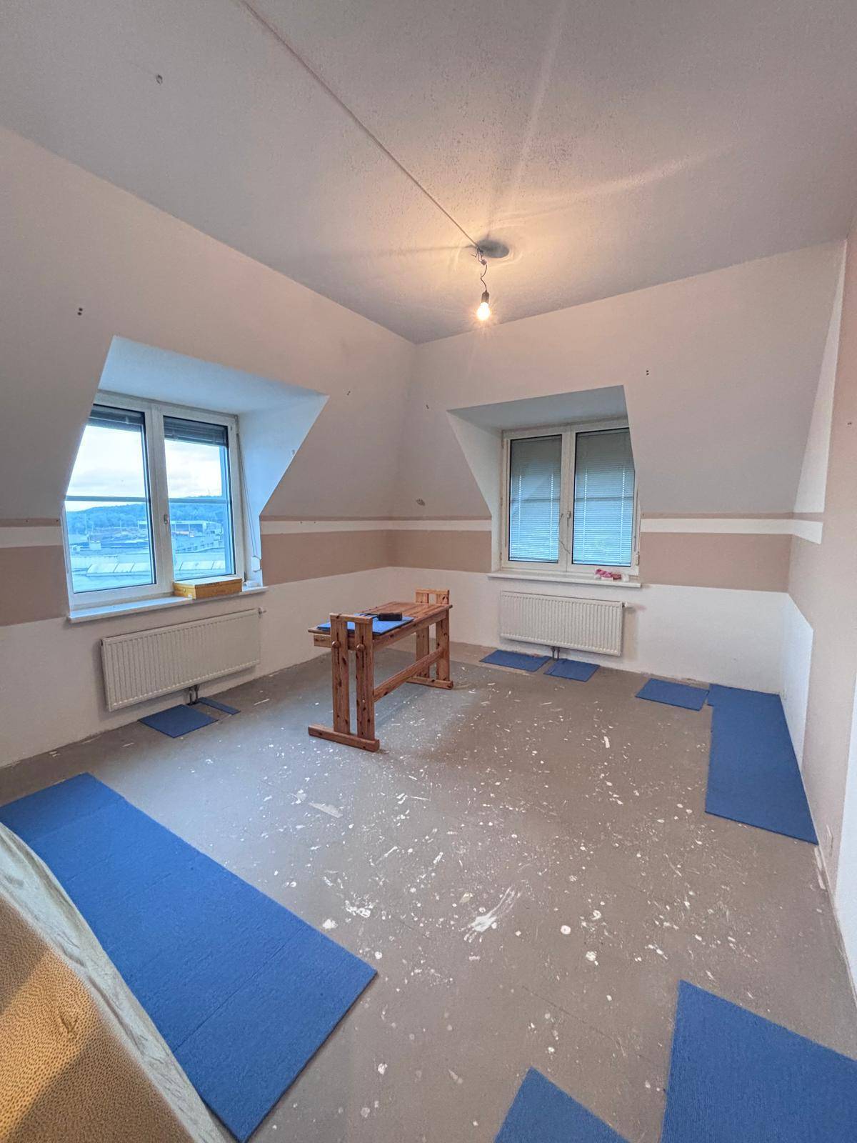 Renovierungsbedürftiger Raum im Dachgeschoss mit Fenstern, Heizkörpern und vorbereitetem Boden.