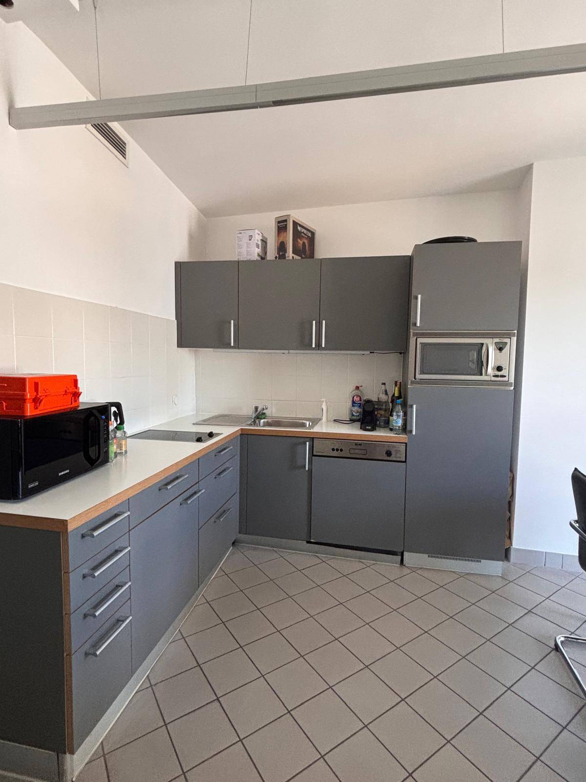 Moderne Küche mit grauen Schränken, Fliesenboden und integrierten Geräten, ideal für den Büroalltag.