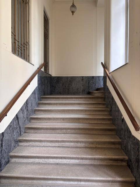 Steintreppe mit Holzgeländer und Marmorverkleidung in einem historischen Gebäude, die nach oben führt.