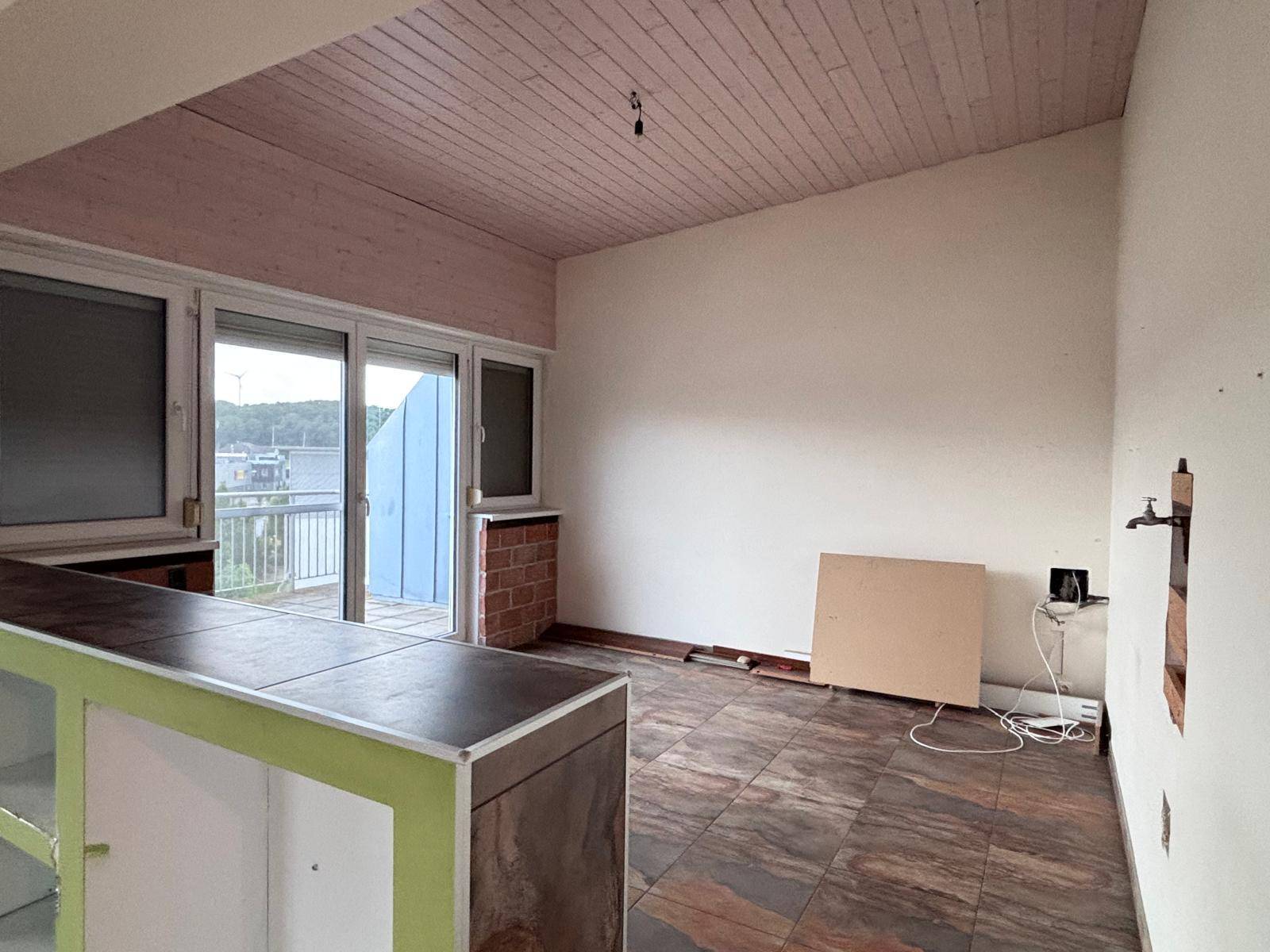 Raum mit Holzdielen an der Decke, Fliesenboden und Zugang zu einem Balkon mit Ausblick.
