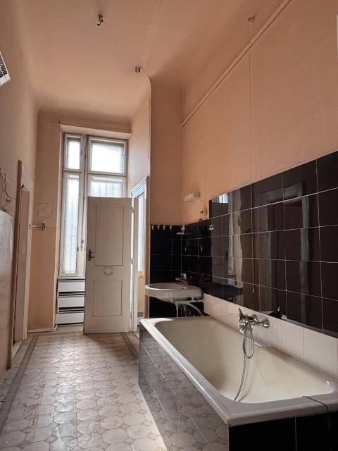 Langes Badezimmer mit Badewanne, Waschbecken und Fenster, das eine umfassende Renovierung benötigt.