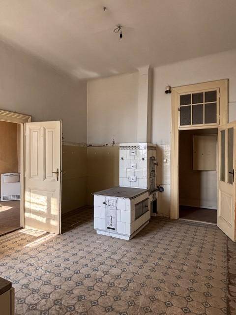 Geräumige Küche mit traditionellem Kachelofen und Fliesenboden, die eine umfassende Renovierung benötigt.