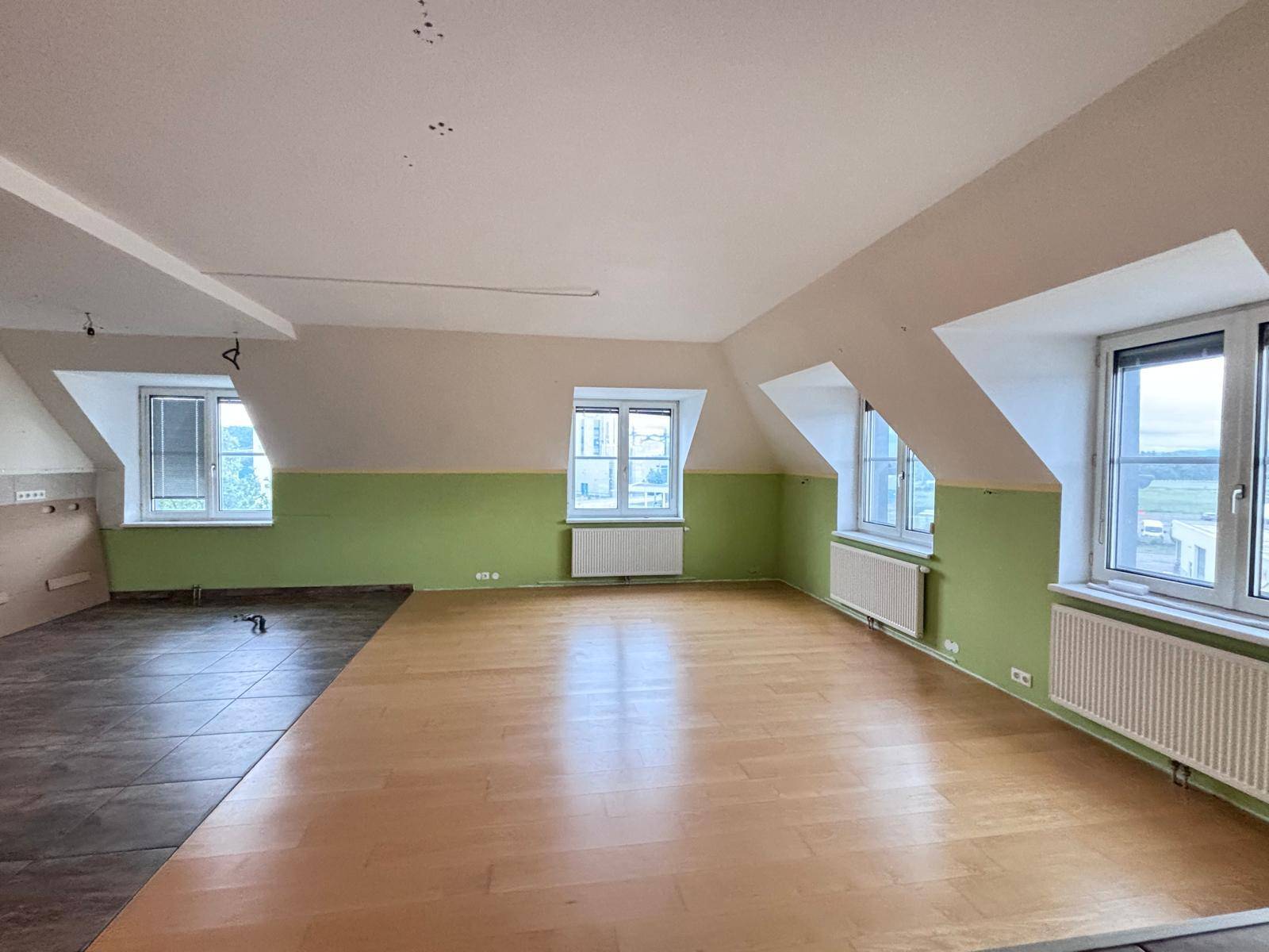 Heller Dachgeschossraum mit Holzboden, grünen Wänden und mehreren Fenstern, bereit zur Gestaltung.