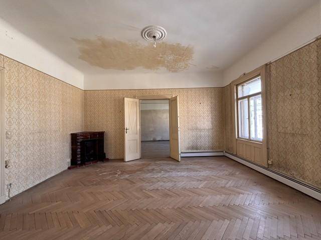 Geräumiges Zimmer mit Fischgrätparkett, Kamin und Stuckdecke, das eine umfassende Renovierung benötigt.