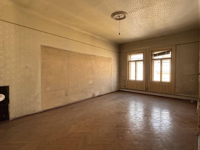 Geräumiges Zimmer mit Fischgrätparkett und zwei hohen Fenstern, das viel Tageslicht bietet.