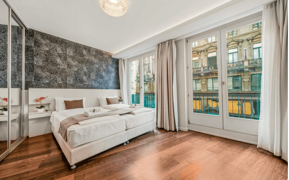 Helles Schlafzimmer mit Doppelbett, verspiegeltem Kleiderschrank und Zugang zu einem französischen Balkon.
