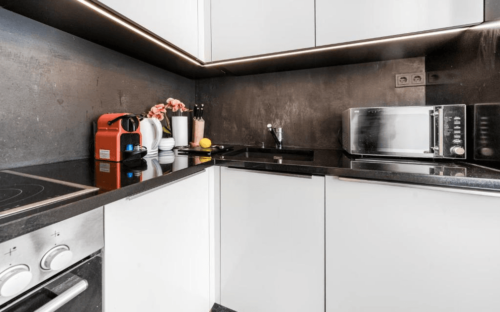 Moderne Küche mit weißen Hochglanzschränken, schwarzer Arbeitsplatte und integrierten Geräten.