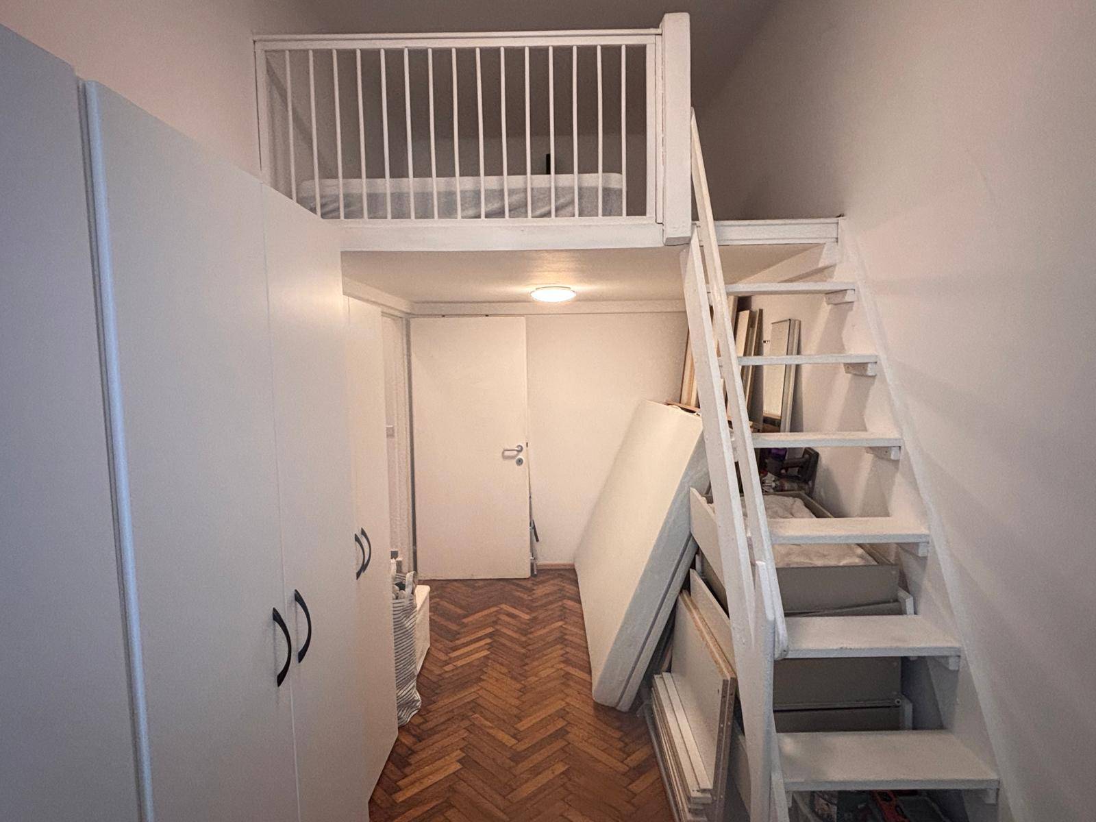 Zimmer mit Hochbett, weißem Kleiderschrank und Holztreppe, ideal für ein kleines Schlafzimmer.