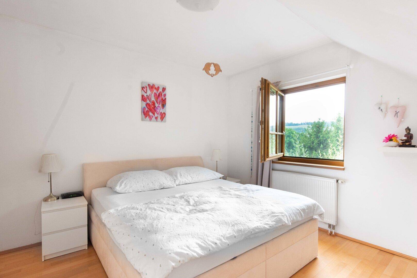 Helles Schlafzimmer im Dachgeschoss mit Holzboden, Doppelbett und weitem Blick in die Landschaft.