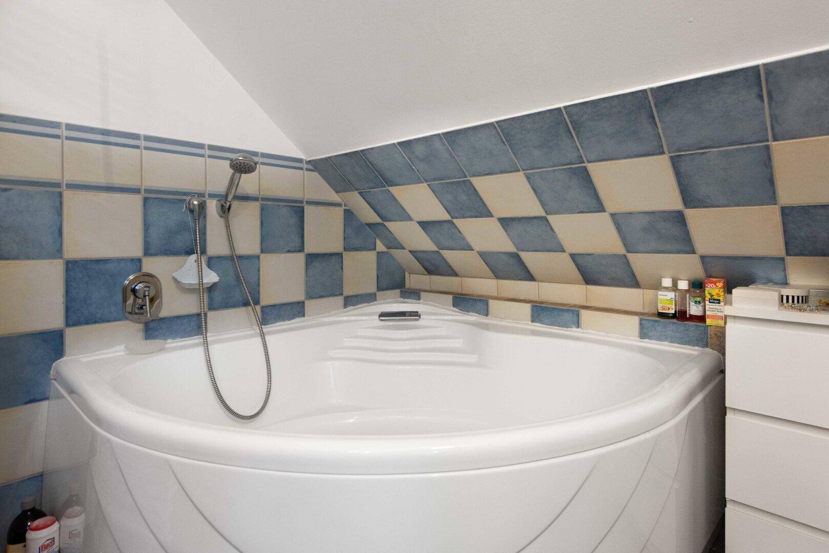 Badezimmer im Dachgeschoss mit Eckbadewanne und charakteristischen blau-weißen Fliesen.