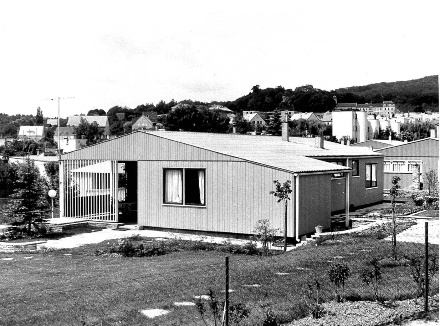 Schwarz-Weiß-Aufnahme eines Bungalows aus den 60er Jahren mit Satteldach und einfacher Architektur in ländlicher Umgebung.