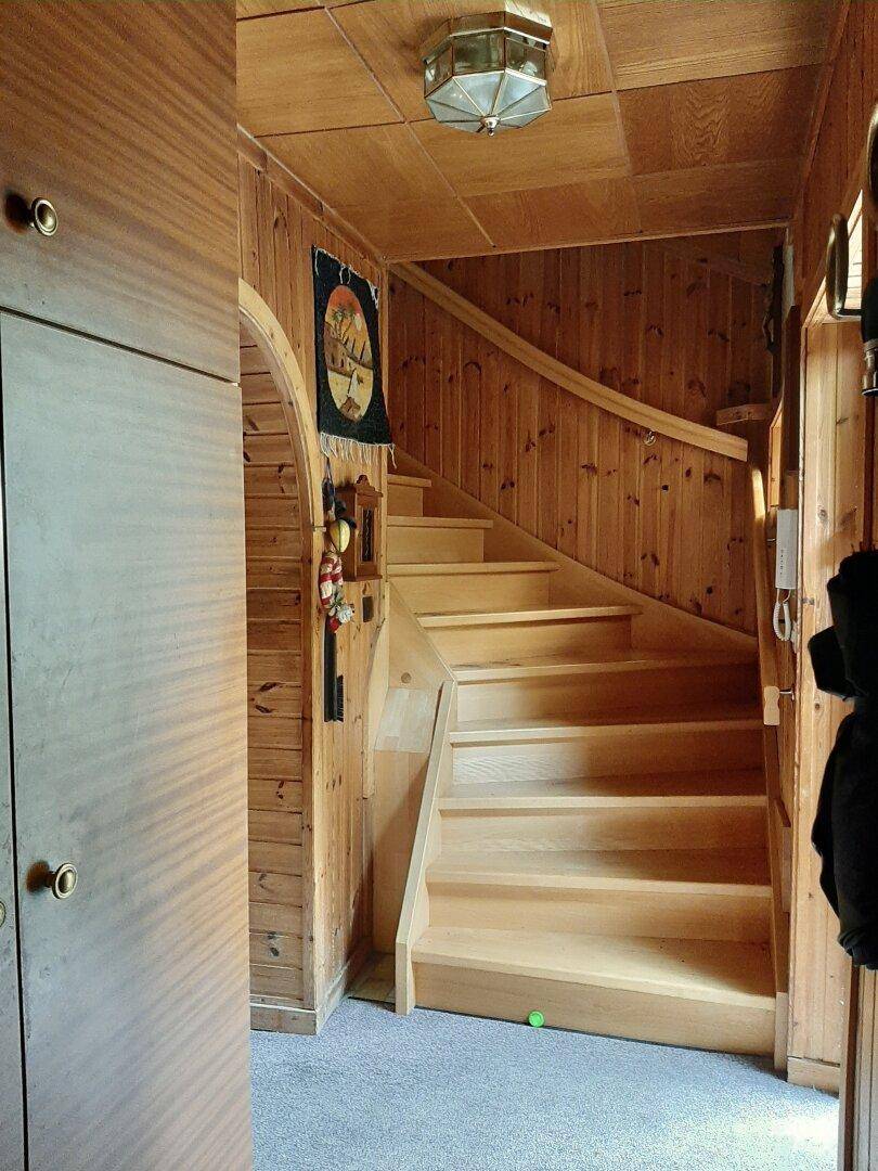 Hölzerne Treppe in einem Flur mit Holzvertäfelung und traditioneller Deckenlampe.