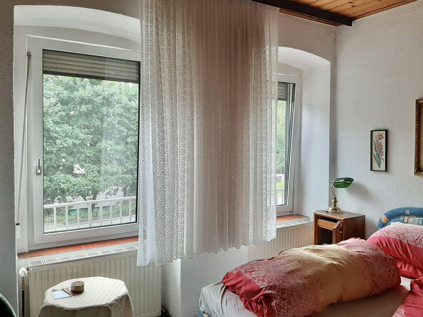 Fenster in einem Schlafzimmer mit Vorhängen, Blick ins Grüne und Heizkörper.