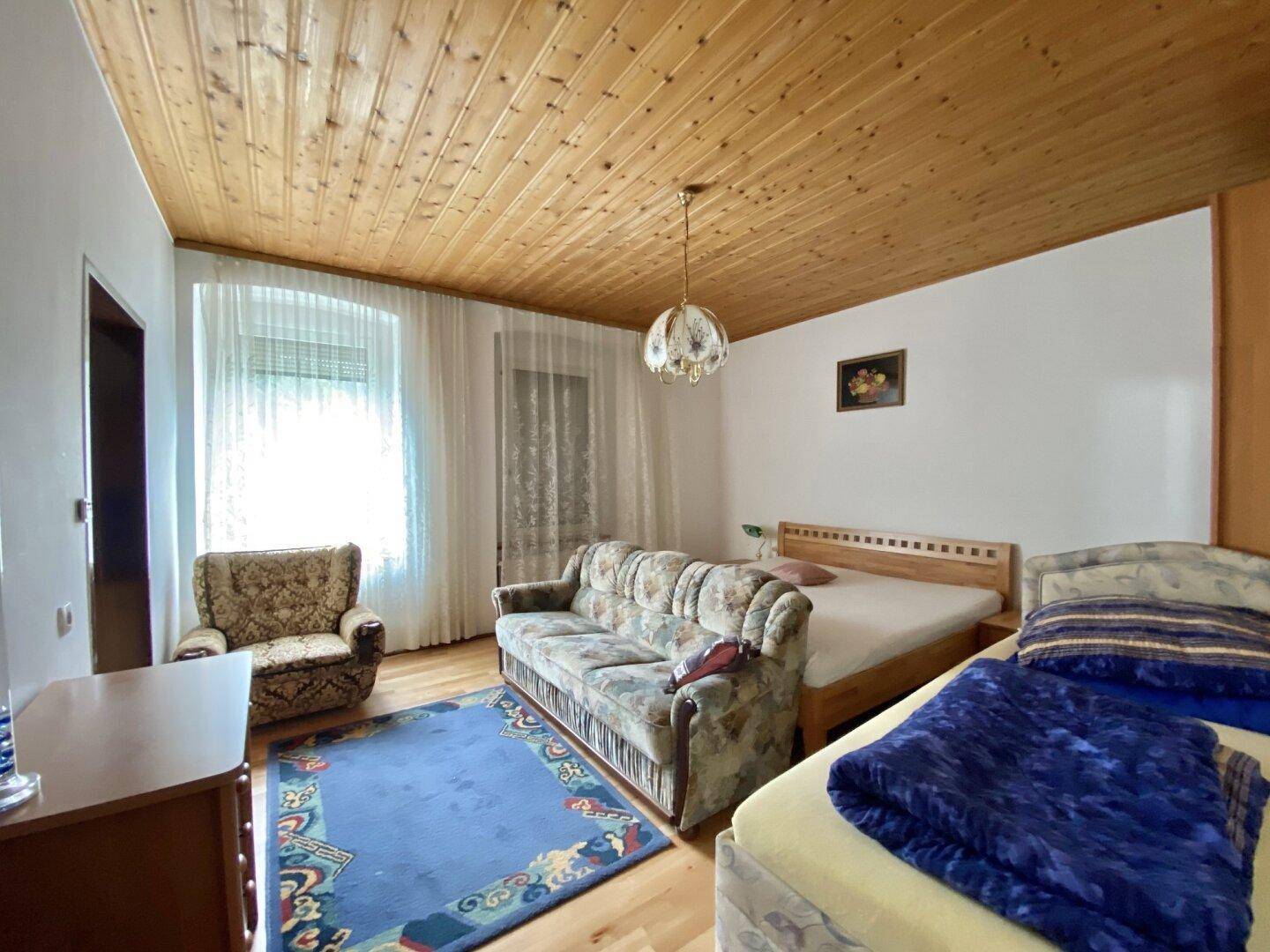 Geräumiges Wohnzimmer mit Holzdecke, Sofa, Bett und Blick auf den Garten.
