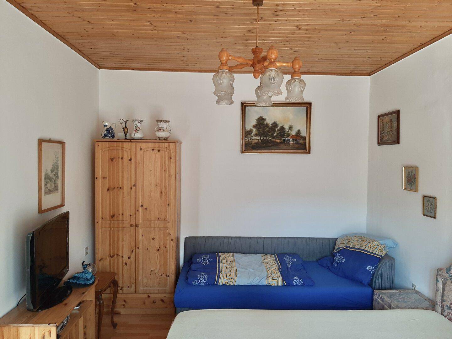 Schlafzimmer mit Einzelbett, Holzschrank, Holzdecke und traditioneller Einrichtung.