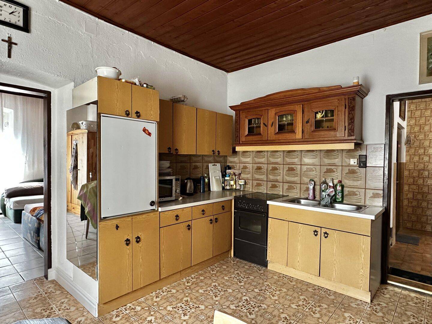 Ältere Küche mit Holzschränken, Fliesenboden und integrierten Geräten.