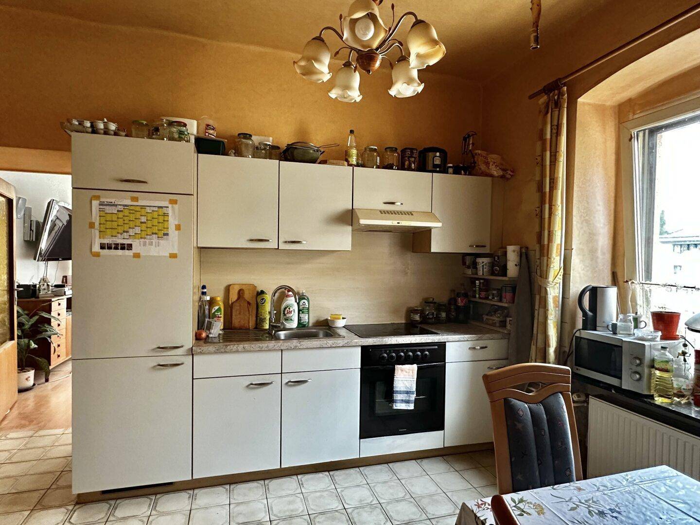 Küche mit weißen Schränken, Essbereich und Fenster, das viel Tageslicht hereinlässt.