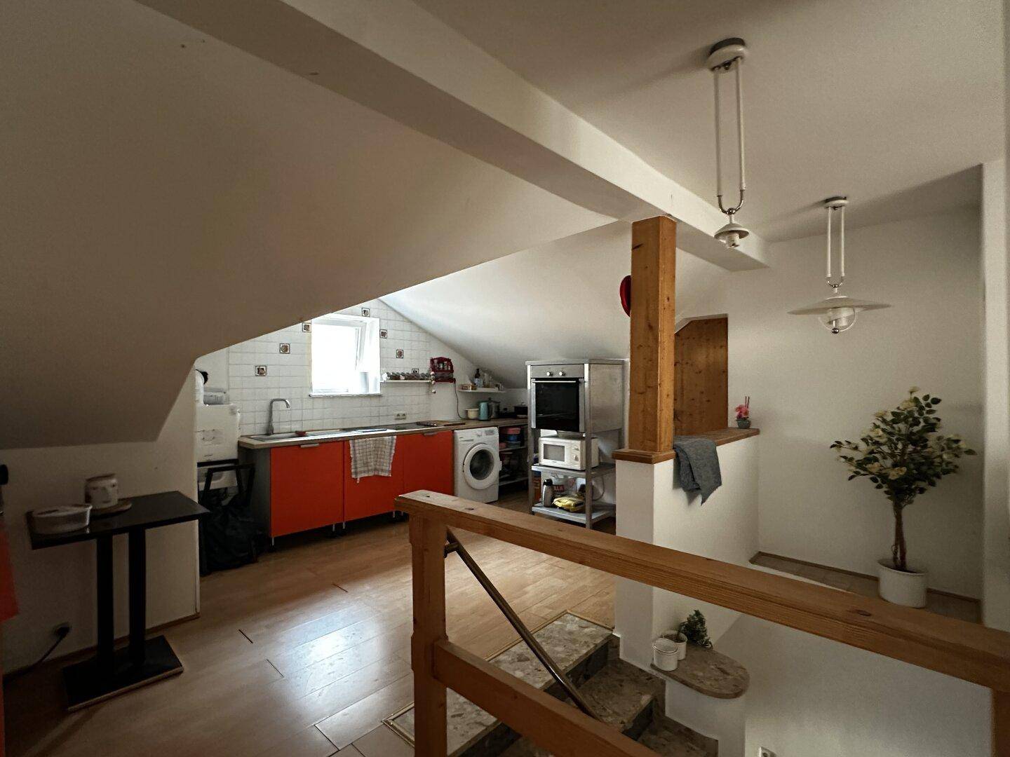 Helle Dachgeschossküche mit roten Schränken, Waschmaschine und sichtbaren Holzbalken.