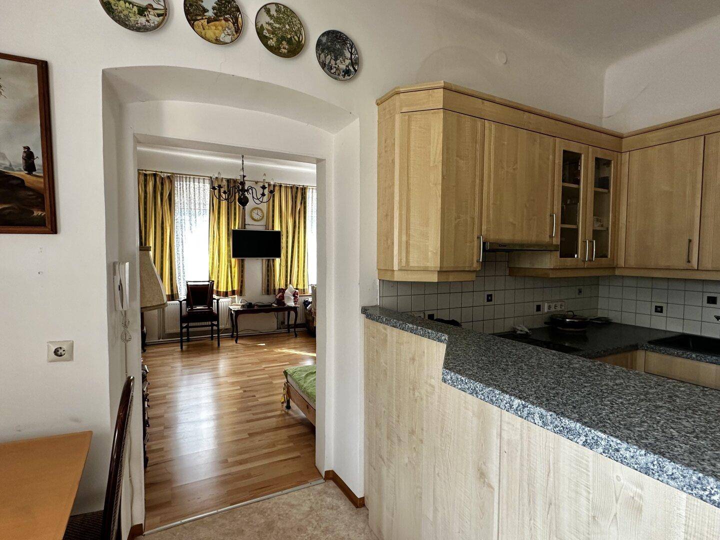 Küche mit Granitarbeitsplatte und Durchgang zum Wohnzimmer mit Holzfußboden und Vorhängen.