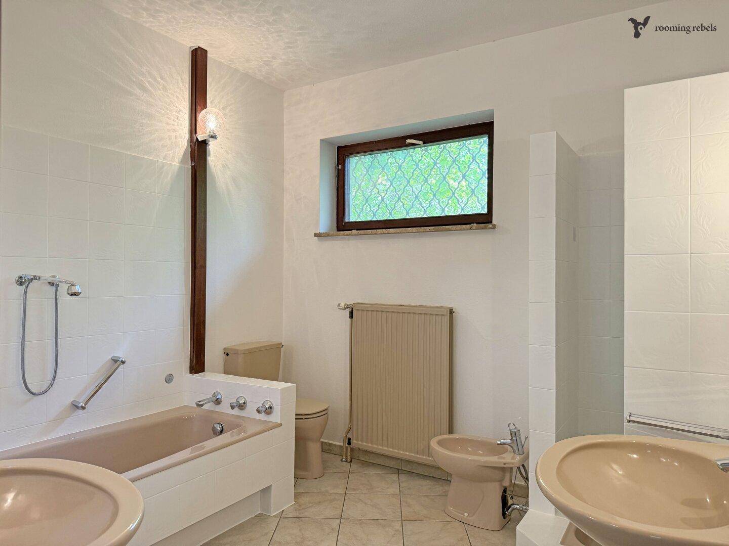 Badezimmer mit beiger Badewanne, WC, Bidet und Fenster.