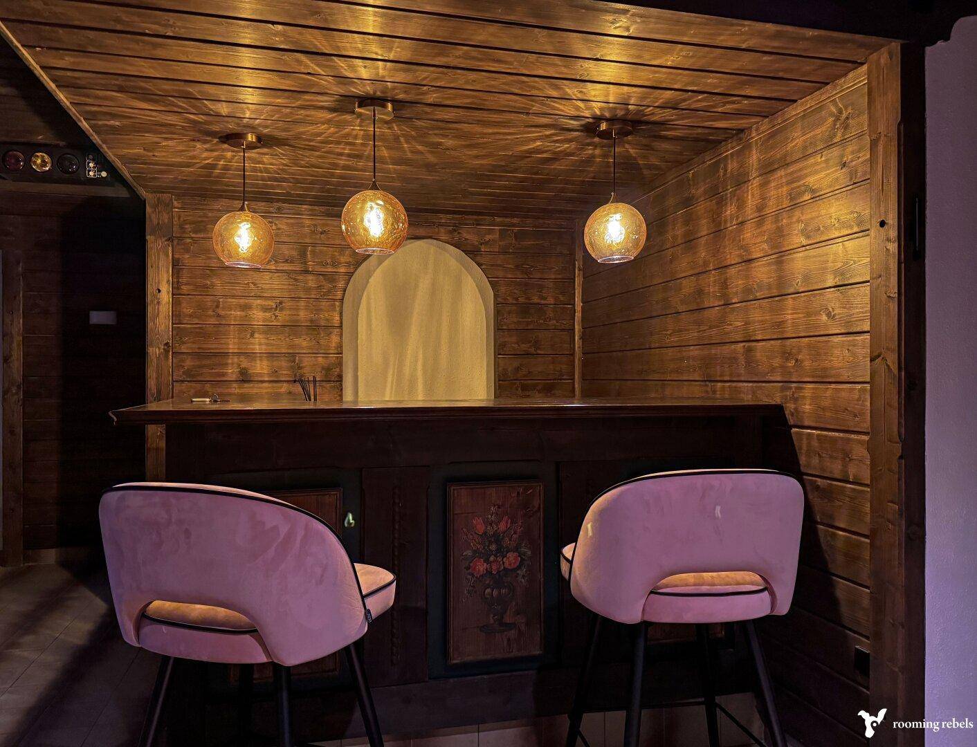 Gemütliche Bar mit Holzverkleidung, Hockern und indirekter Beleuchtung.