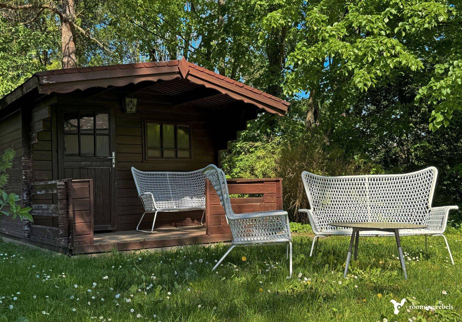 Kleines Gartenhaus mit Sitzgelegenheiten auf einer grünen Wiese.