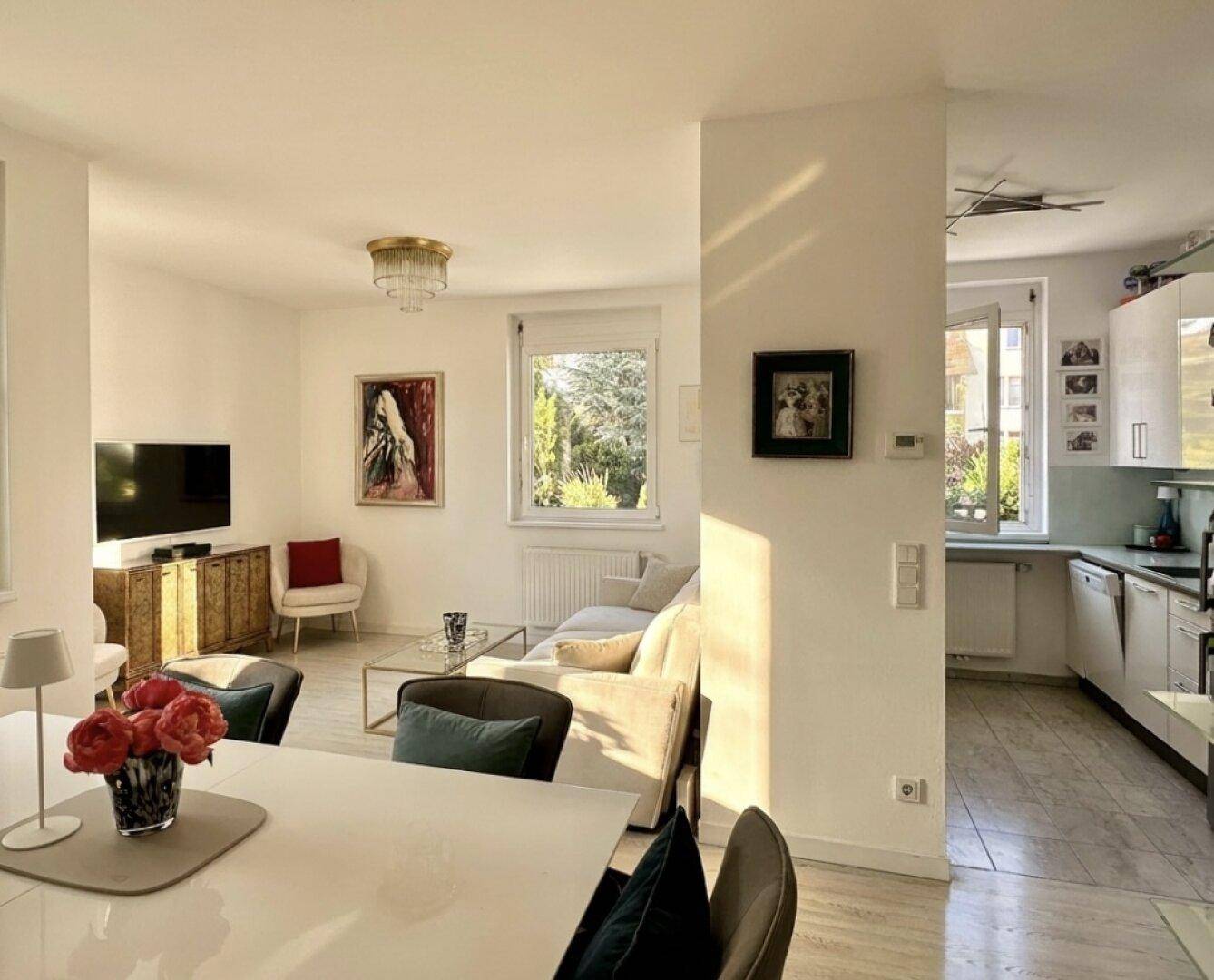 Heller Wohn- und Essbereich mit Sofa, Esstisch und Blick ins Grüne sowie zur Küche.