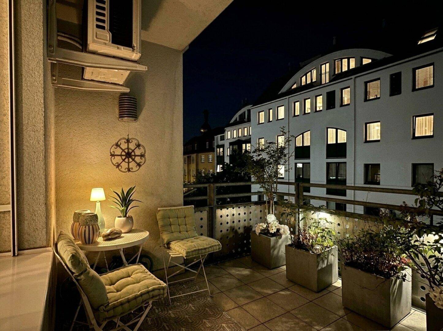 Abendliche Atmosphäre auf dem Balkon mit beleuchteten Pflanzen und Blick auf die Stadt.
