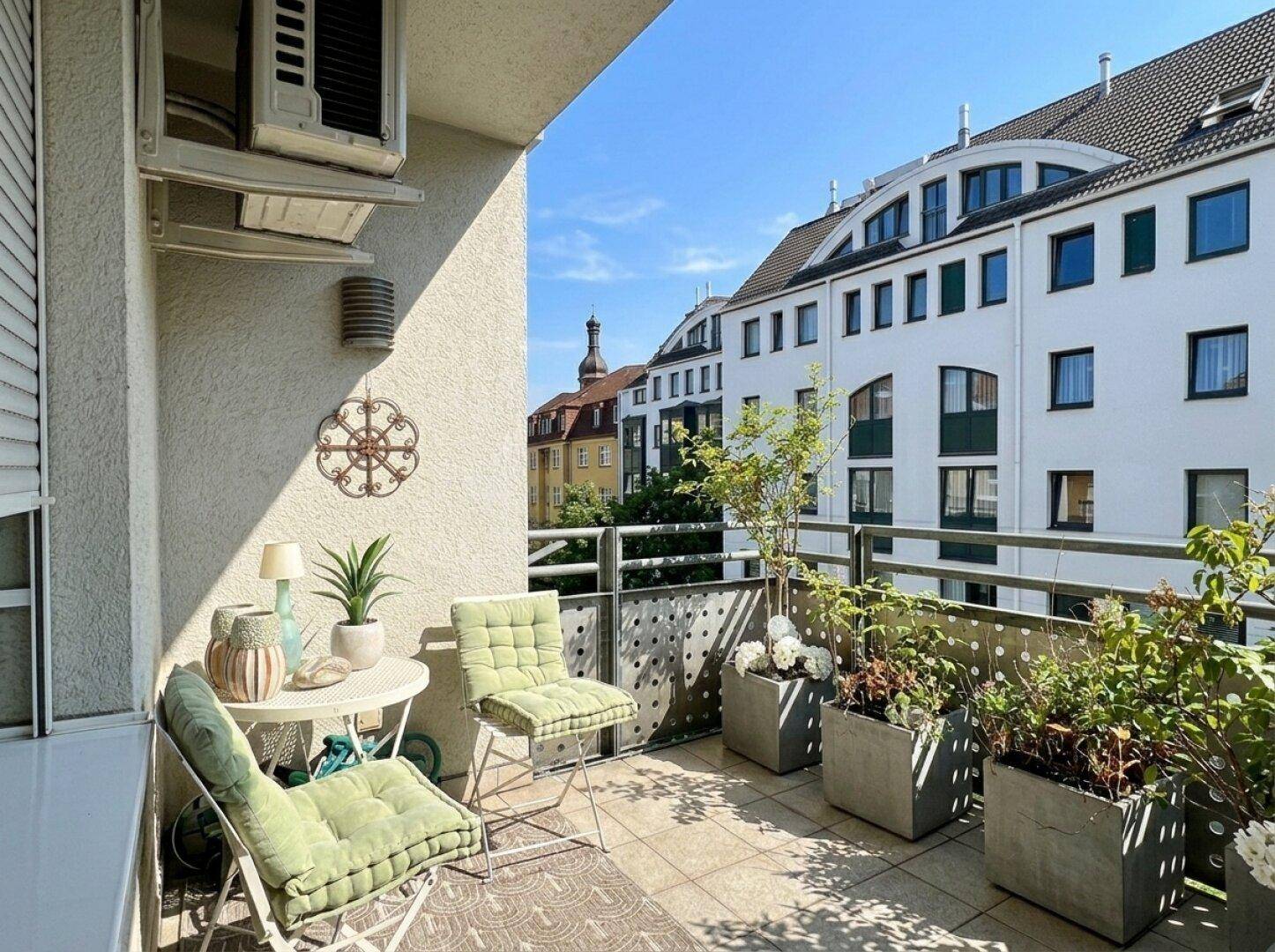 Sonniger Balkon mit Sitzgelegenheiten, Pflanzen und Blick auf die umliegenden Gebäude.