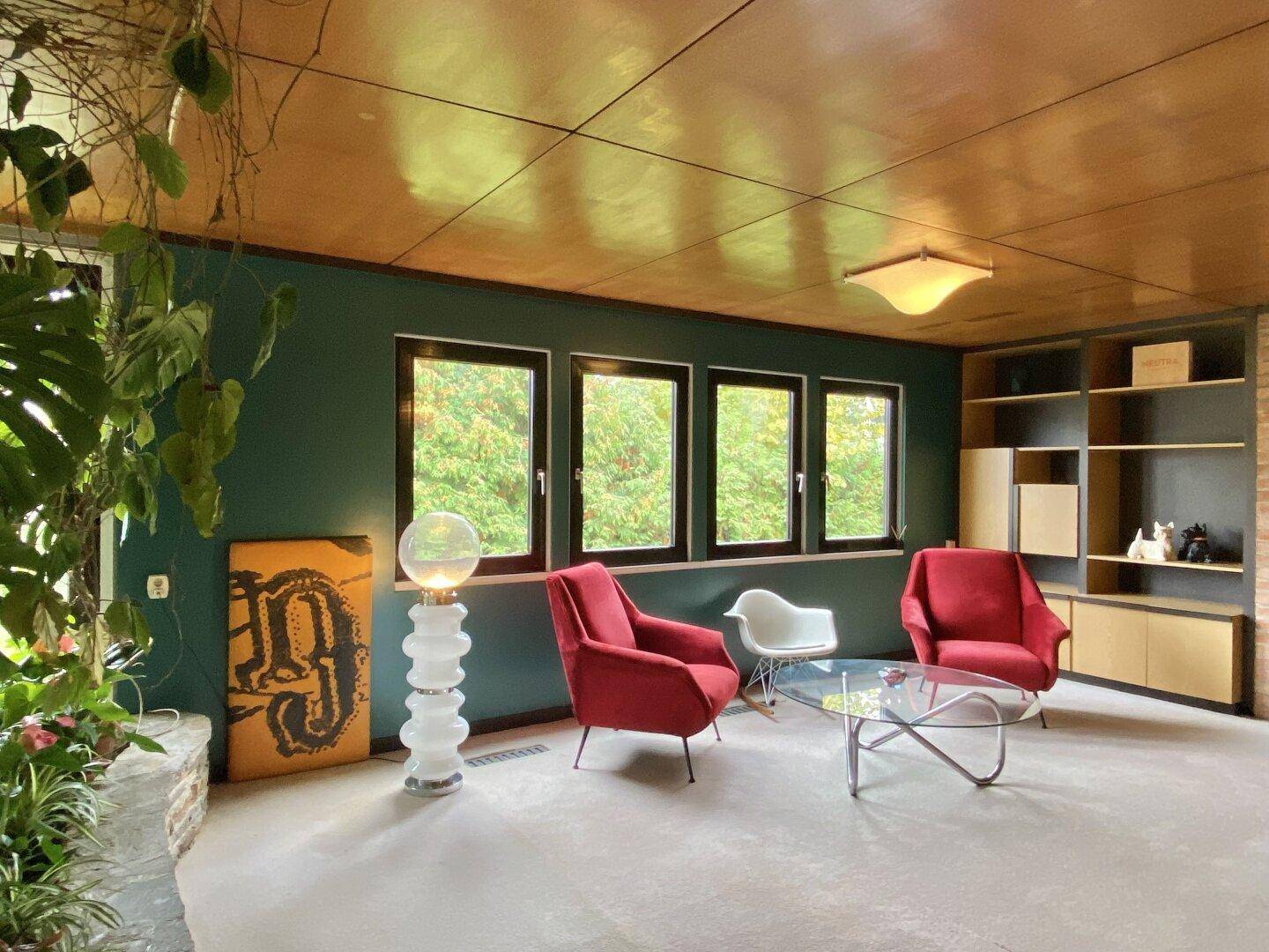 Gemütliches Wohnzimmer mit dunkelgrünen Wänden, Holzdecke und Blick ins Grüne.