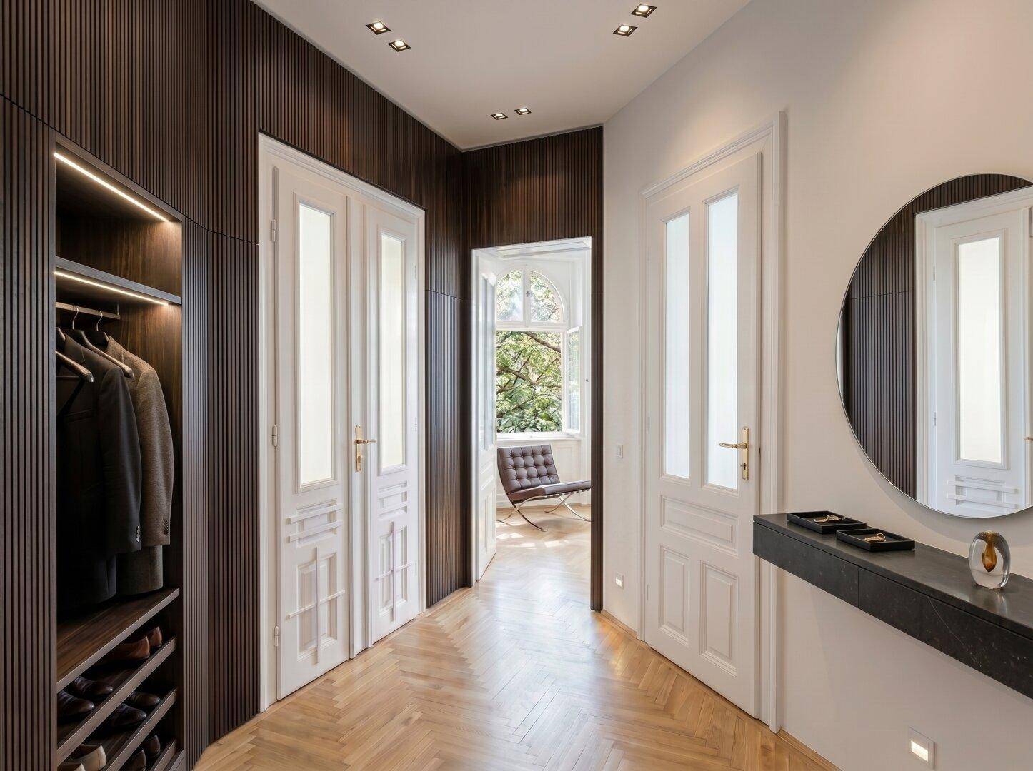 Eleganter Flur mit integriertem Kleiderschrank, Fischgrätparkett und Blick in einen hellen Raum.