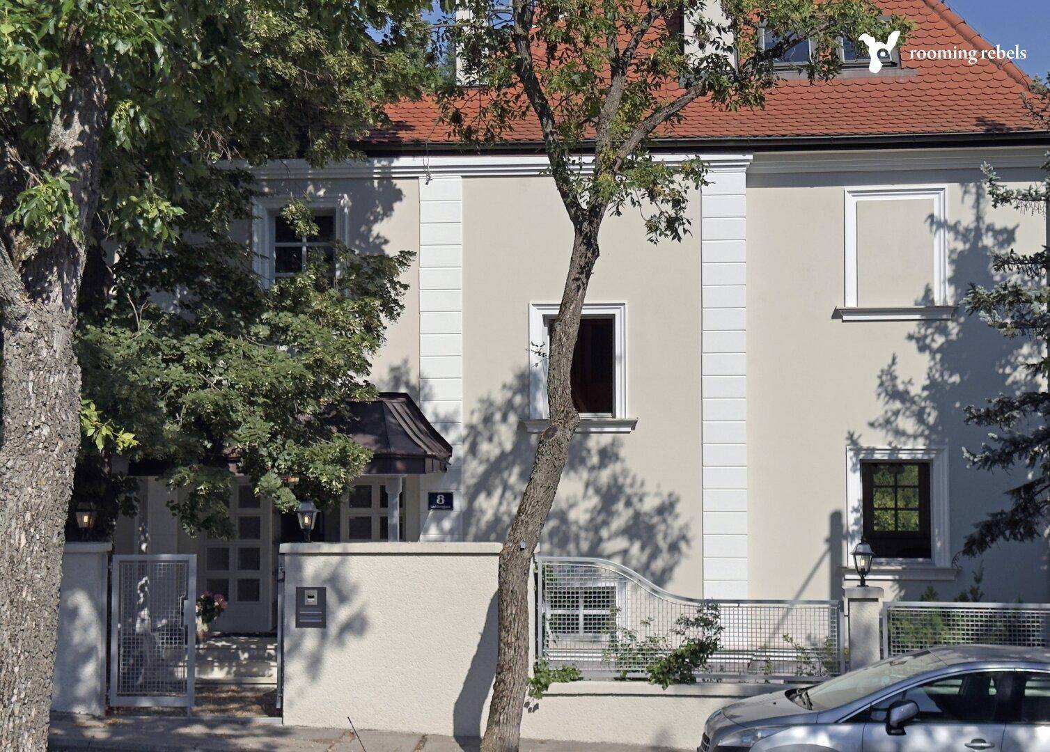 Elegante Fassade des Hauses mit klassischer Architektur und einem Baum im Vordergrund an der Straße.