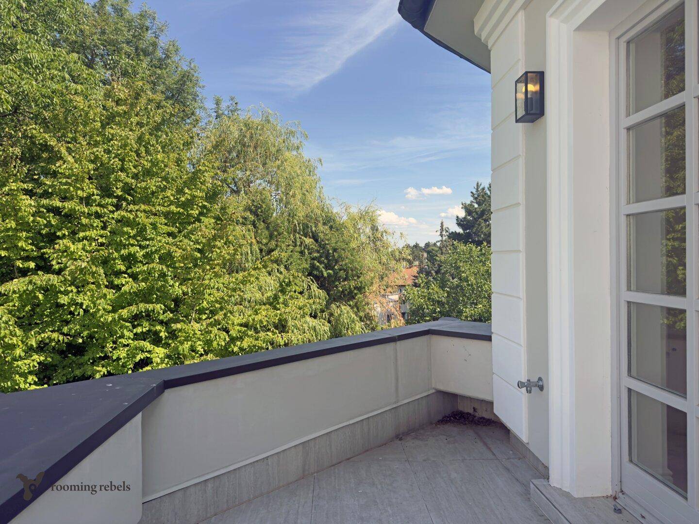 Balkon mit heller Brüstung und weitem Blick auf grüne Bäume und die umliegende Landschaft.