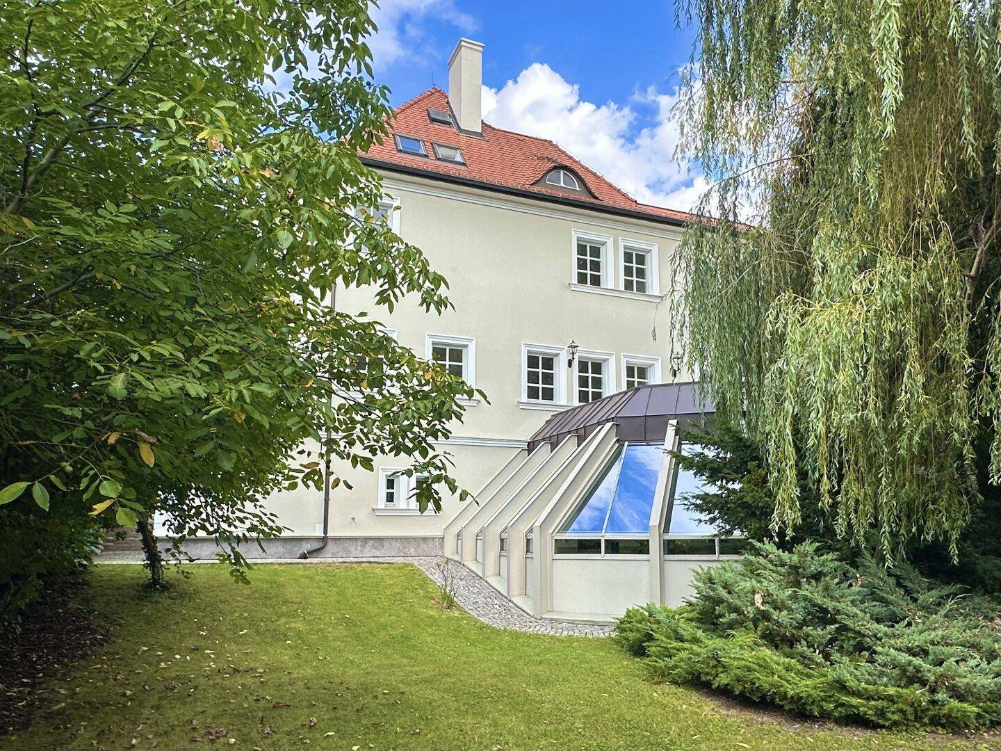 Seitenansicht des Hauses mit Garten, Rasenfläche und einem modernen Anbau für den Poolbereich.