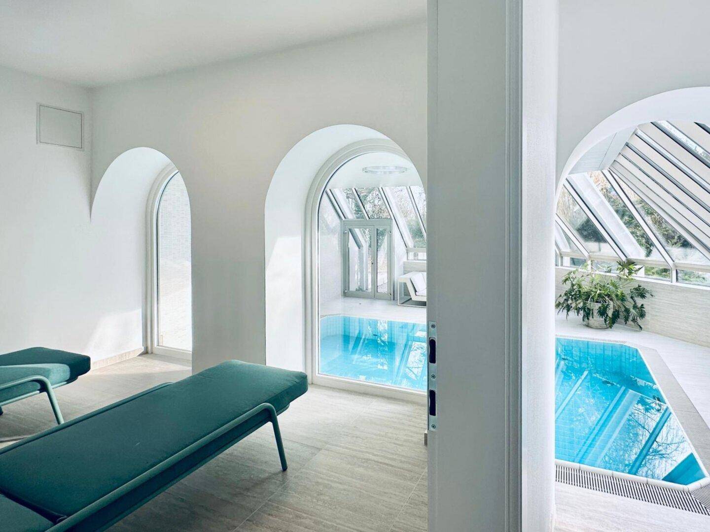 Heller Wellnessbereich mit Innenpool, Liegestühlen und großen Bogenfenstern für Entspannung.