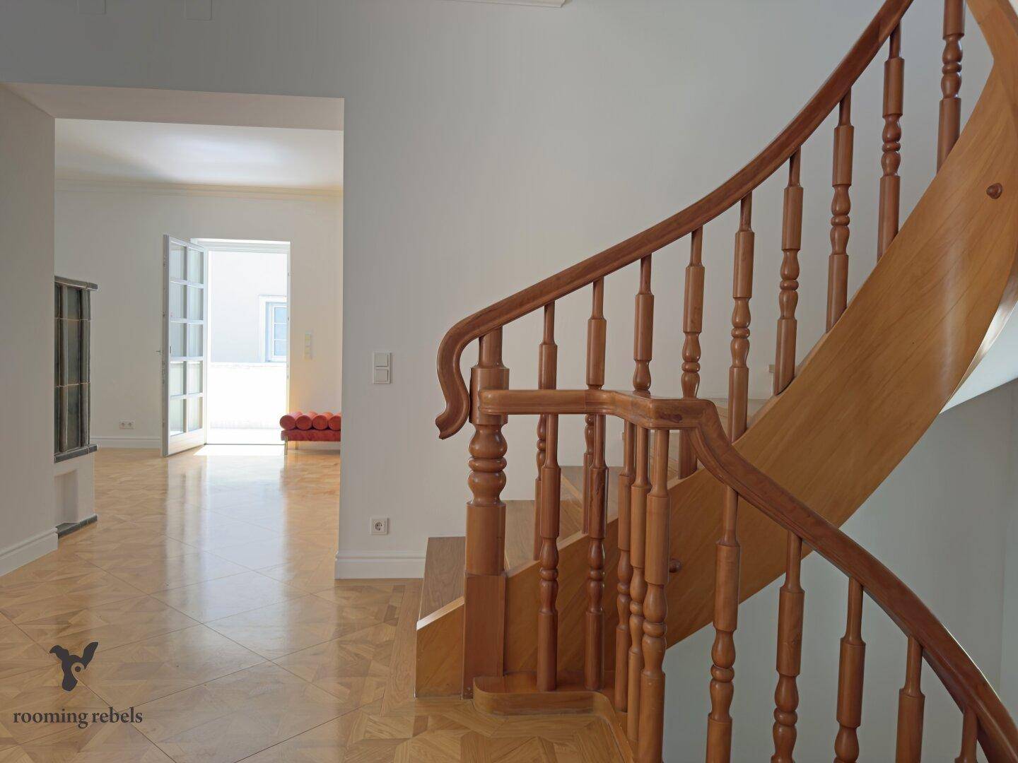 Heller Eingangsbereich mit eleganter Holztreppe und klassischem Parkettboden.