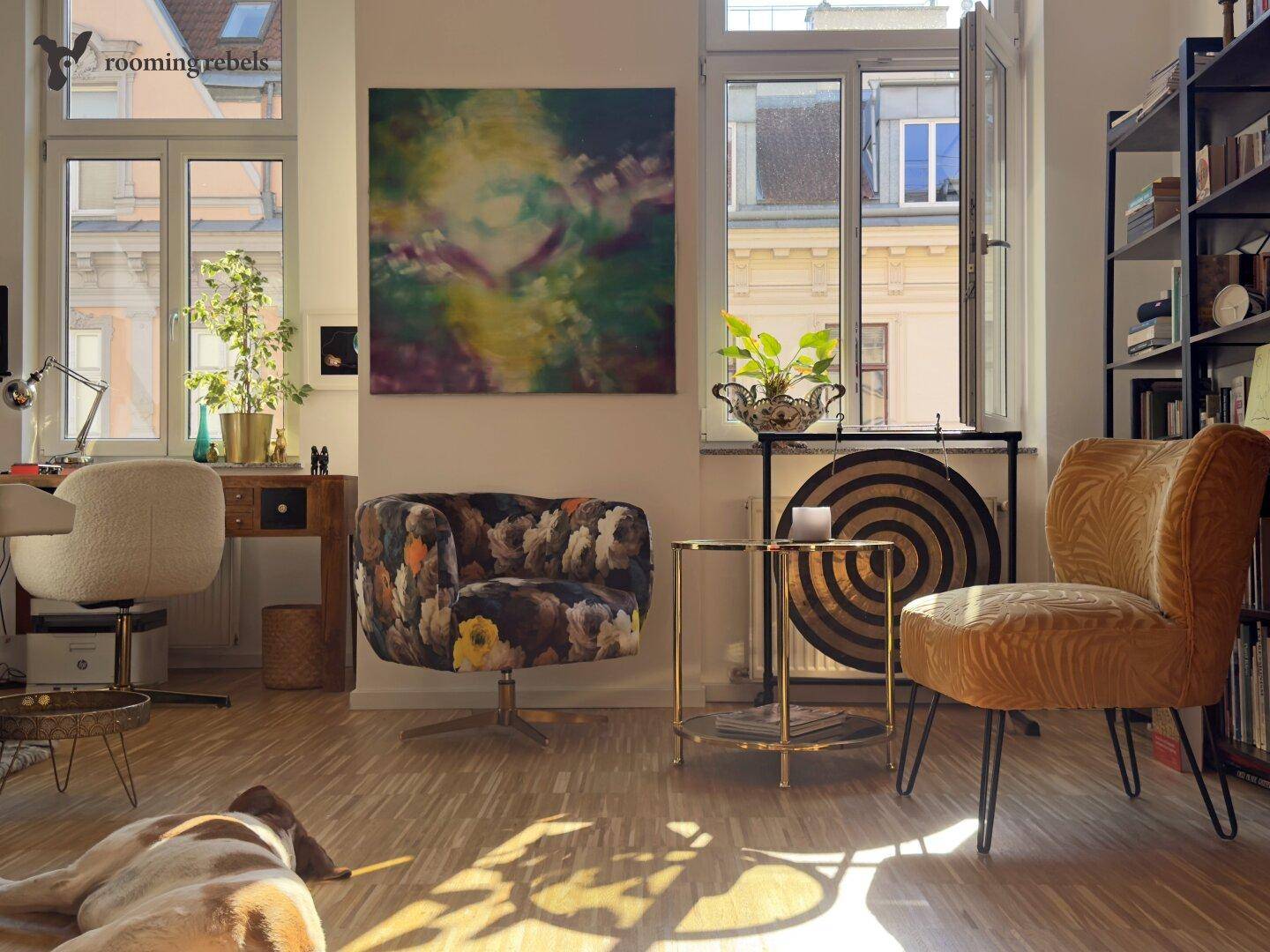 Geräumiges Wohnzimmer mit Holzboden, Bücherregal und viel Tageslicht, ein Hund liegt entspannt auf dem Boden.