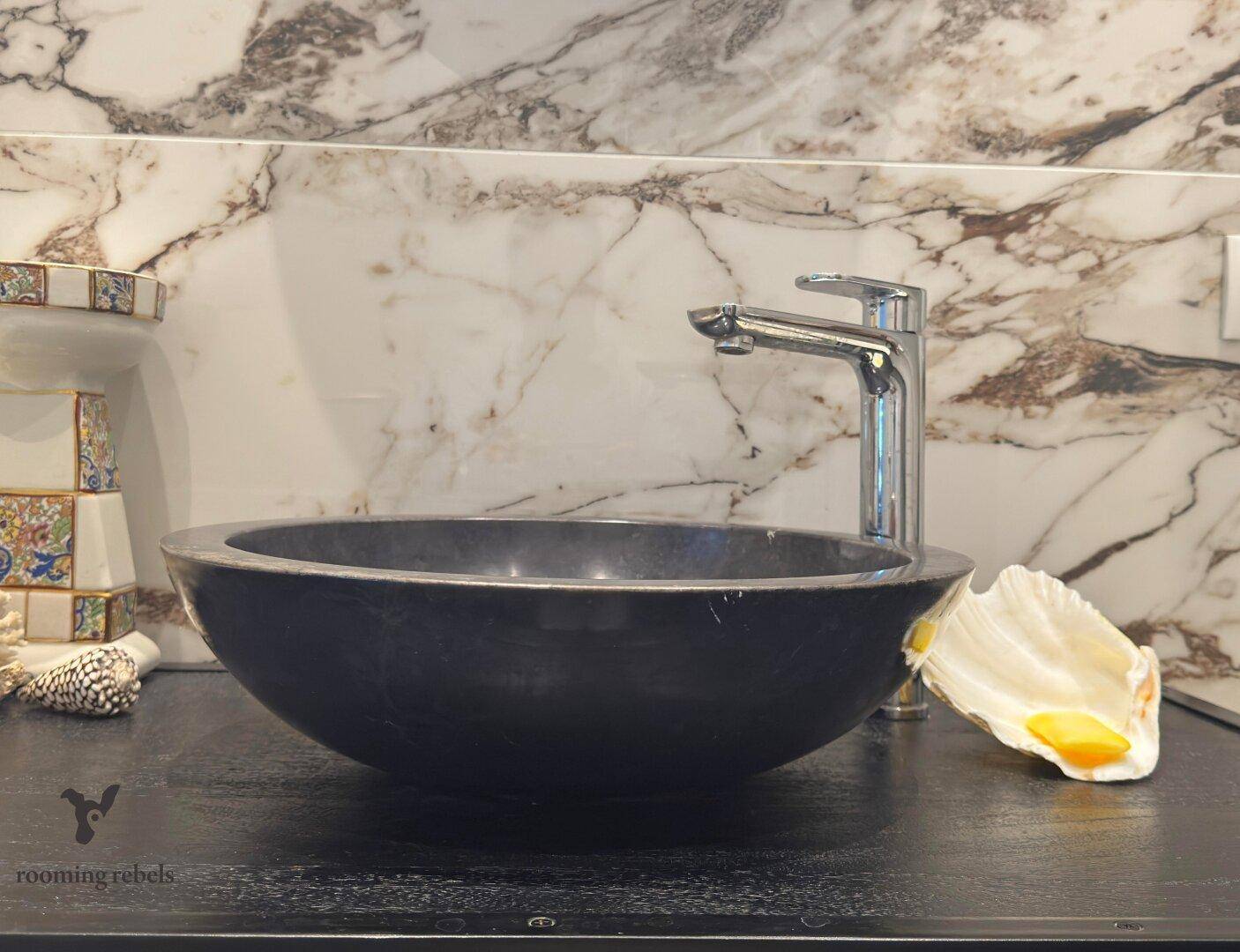 Modernes Badezimmer mit einem eleganten schwarzen Aufsatzwaschbecken und Marmor-Rückwand.