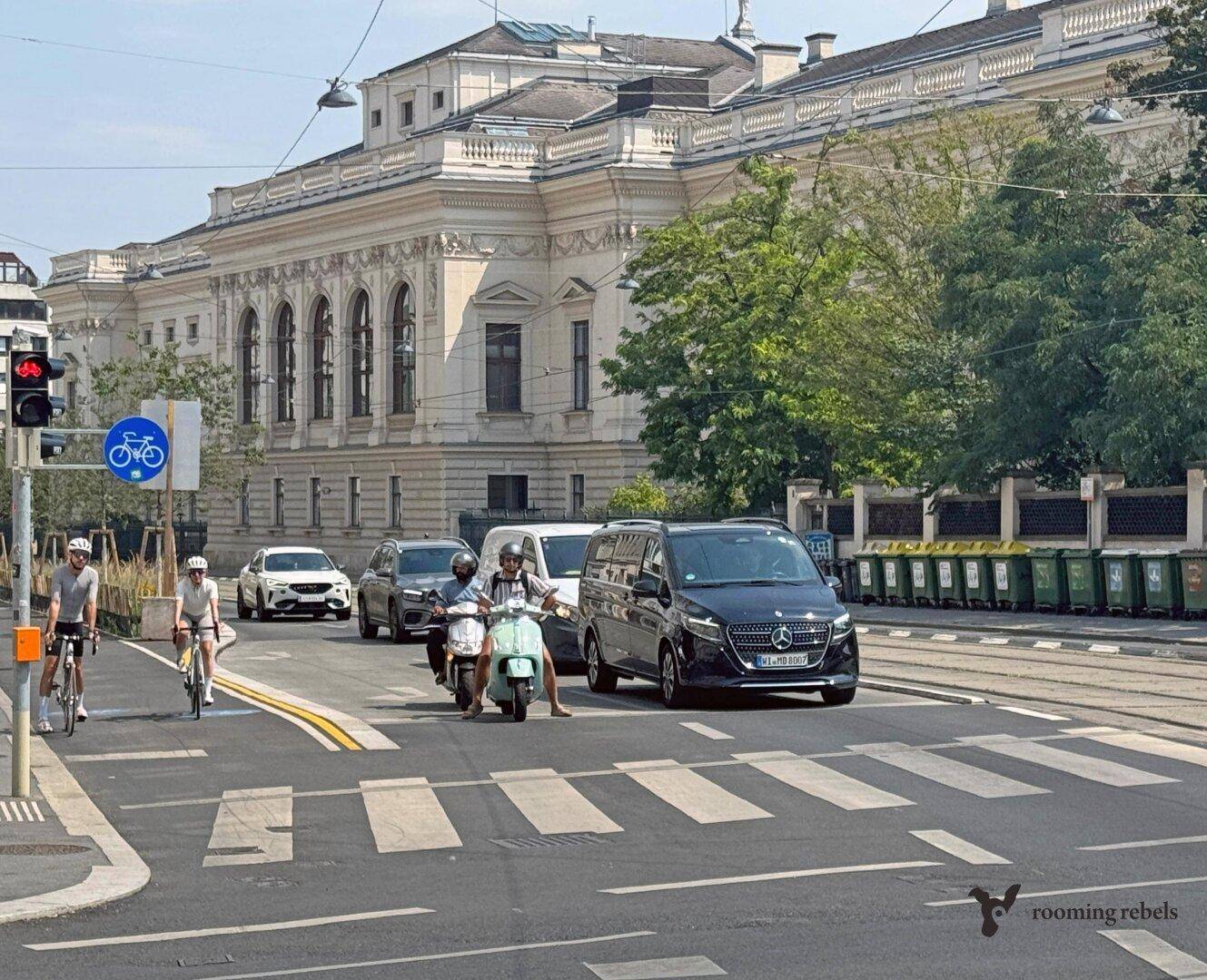 Belebtes Stadtbild mit Verkehr, Fußgängern und einem historischen Gebäude im Hintergrund.