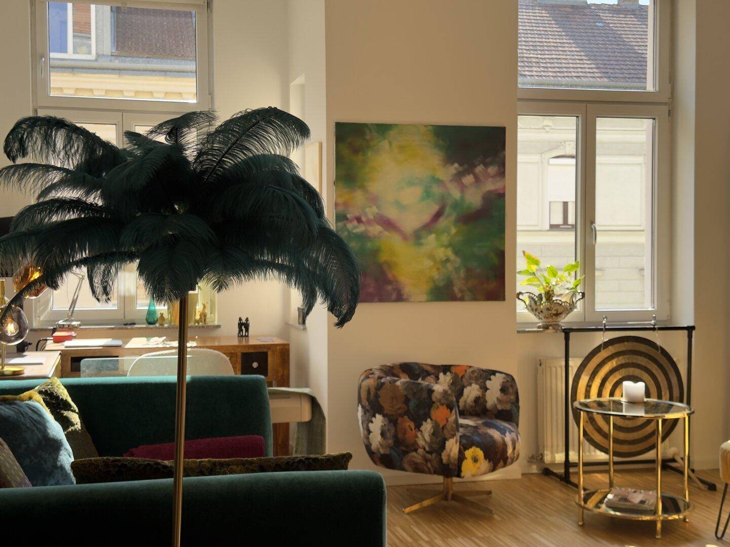 Helles Wohnzimmer mit farbenfroher Kunst, einem Federlampenschirm und einem bequemen Sessel.