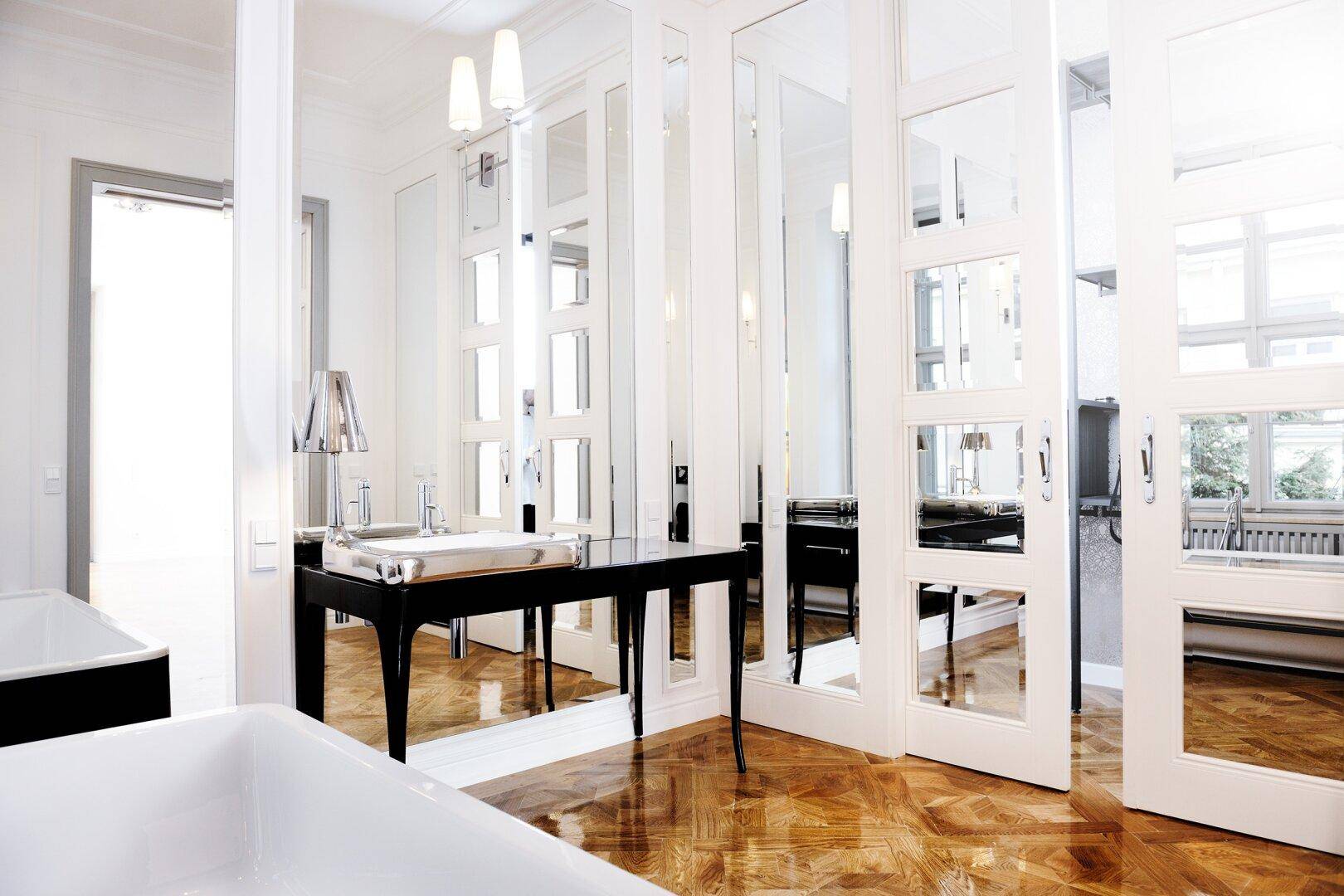 Elegantes Badezimmer mit glänzendem Parkettboden, freistehender Badewanne und Spiegeltüren.
