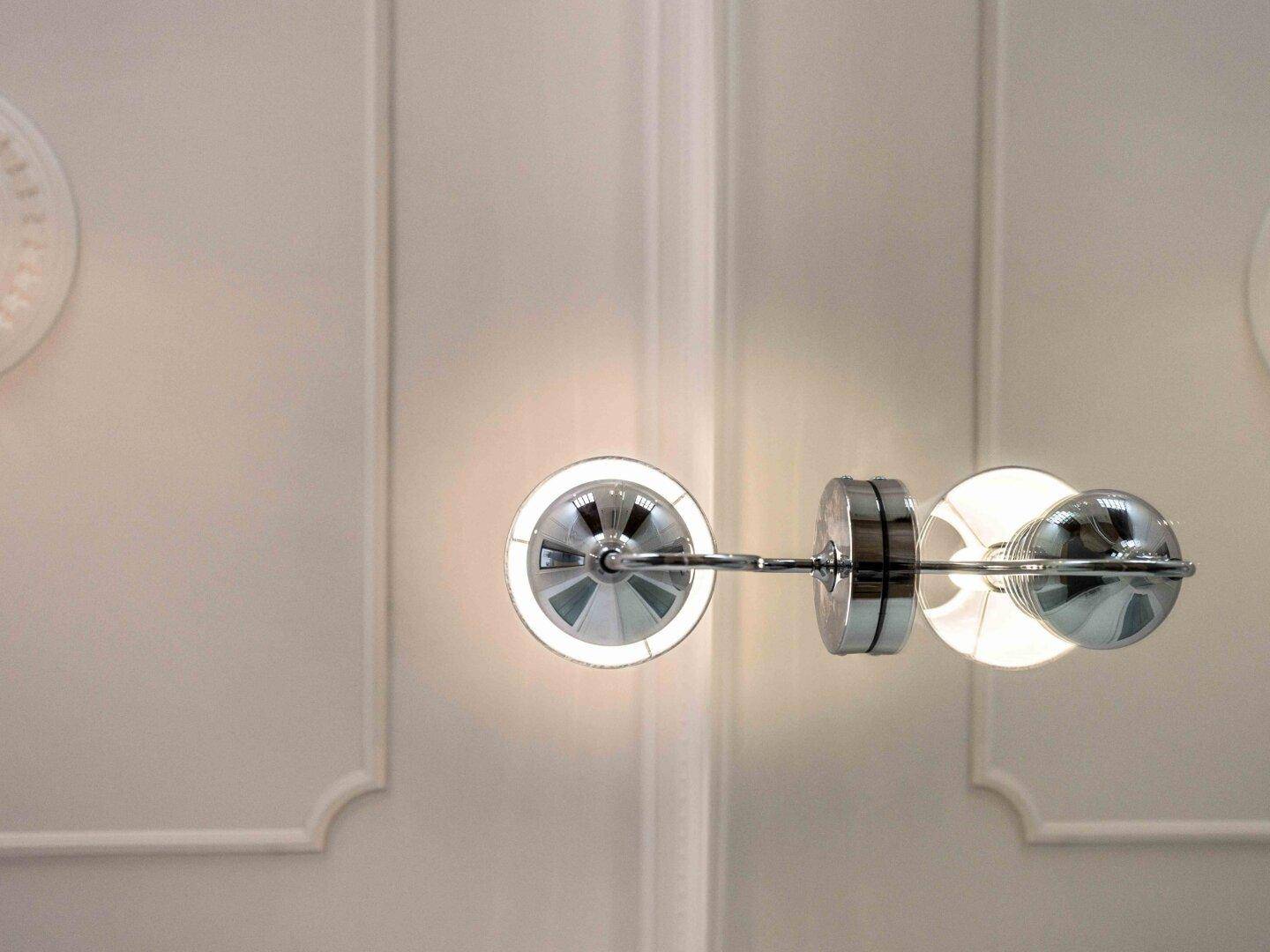 Moderne Wandleuchte mit metallischen Akzenten und indirekter Beleuchtung an einer hellen Wand.