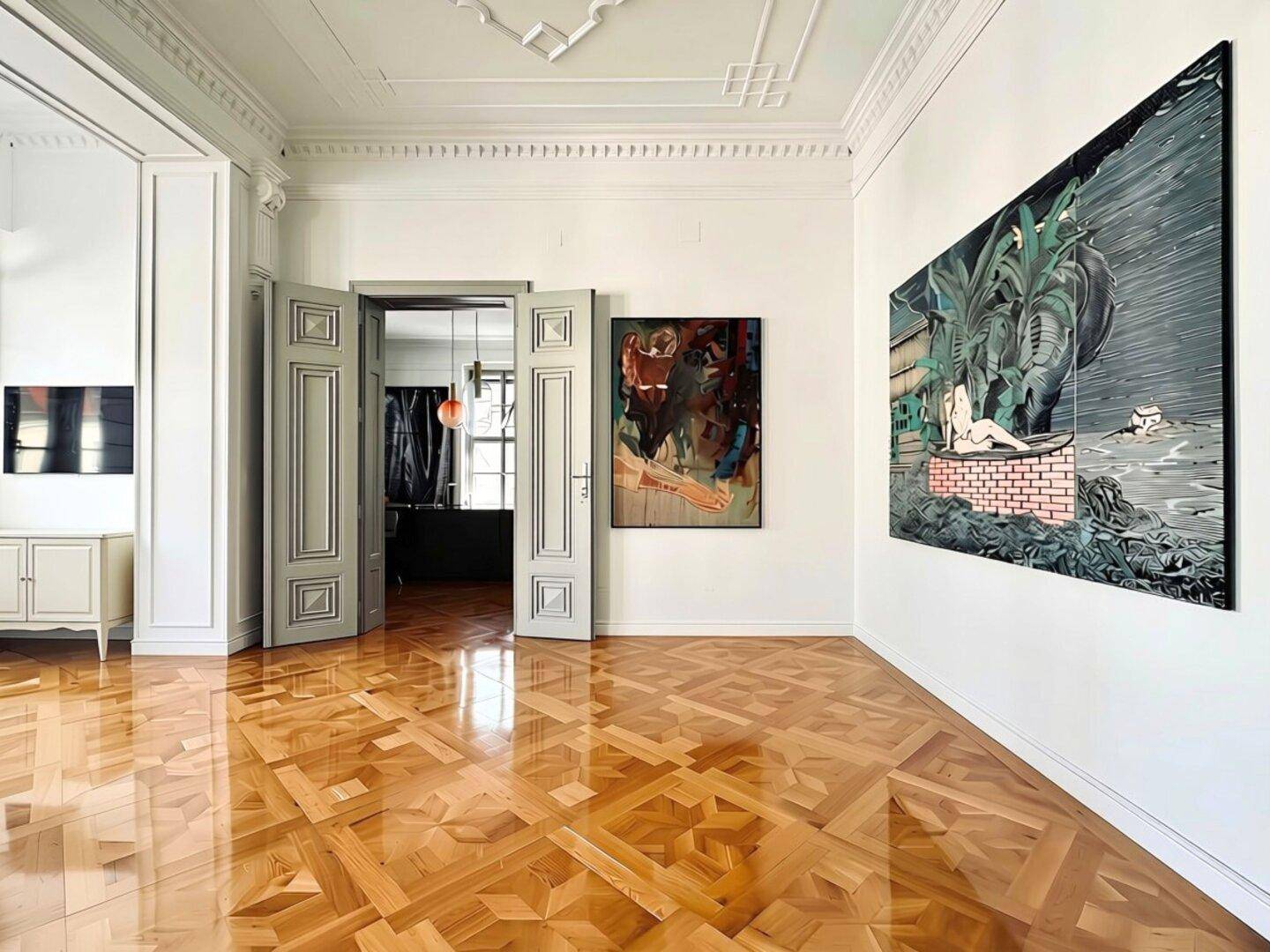 Geräumiger Wohnraum mit Parkettboden, hohen Decken und Kunstwerken an den Wänden, verbunden durch Flügeltüren.